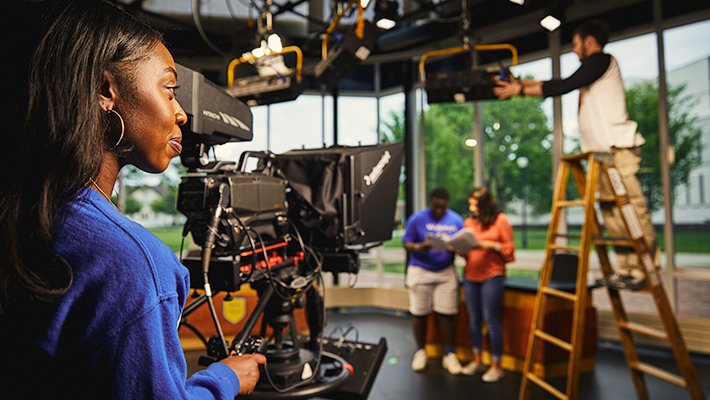 Broadcast commiunication student preparing to film in studio while classmates set up equipment