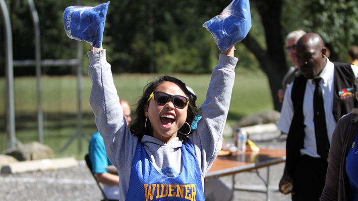Student jumping in the air at Widener homecoming with two giveaways in her hands