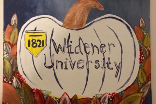 Painting of a pumpkin surrounded by leaves and 'Widener University' and the shield in the center