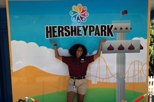 Donya Moore Hershey Park 960 x 640 Student holds hands up above her head to point to a sign that says Hershey Park