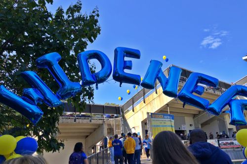 People walking into the stadium on Homecoming, passing beneath an an arch of blue balloons that spell &quot;Widener&quot;
