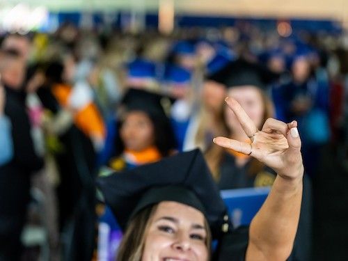 A Widener student gives the peace sign while standing in front of her peers at Commencement