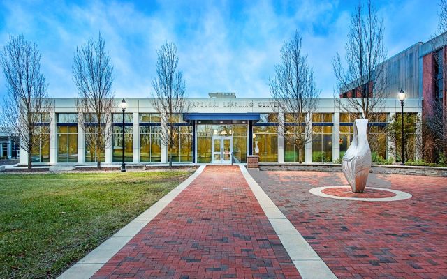Kapelski Hall. The trees are just starting to leaf. There is a brick pathway leading past a brick plaza